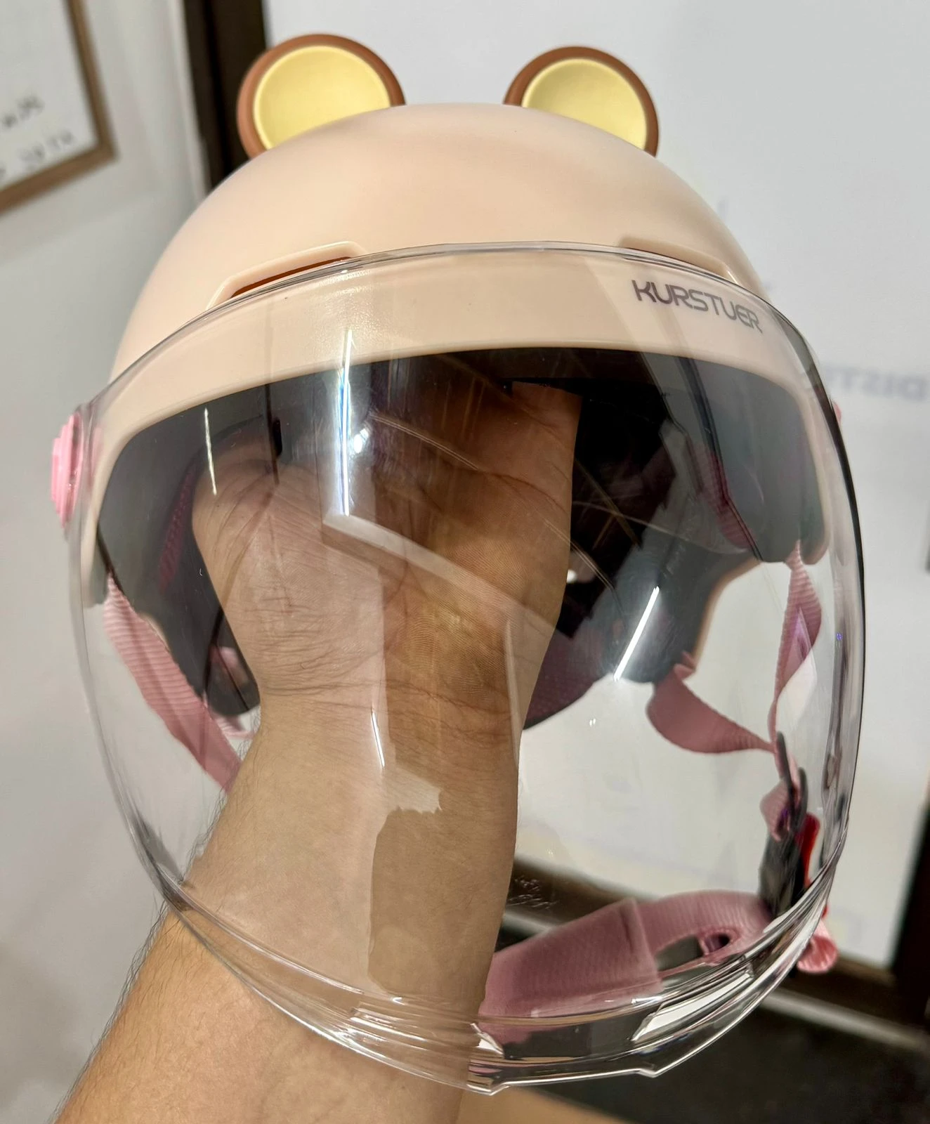 Casco juvenil color beige con orejas de capibara y visor transparente extendido, mostrando detalles internos y sistema de sujeción rosa.