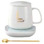 Termo eléctrico de cerámica blanca con base calefactora, incluye taza con asa, logo dorado y cuchara metálica.