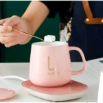 Termo eléctrico de cerámica rosa con base calefactora, en uso para calentar café o té, con logo dorado y tapa removible visible.