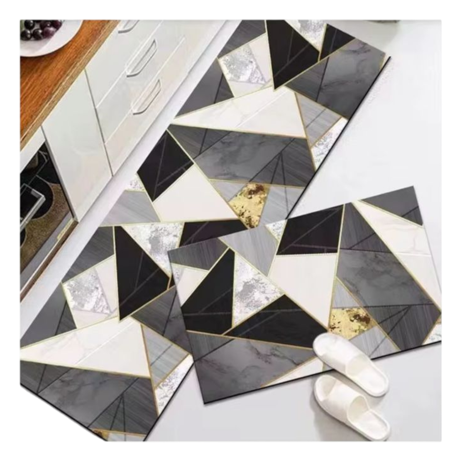 Tapete de cocina antideslizante con diseño geométrico en negro, blanco y gris, con detalles dorados. Se muestra desplegado sobre el suelo junto a un par de sandalias blancas.