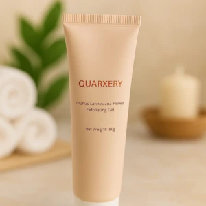 Tubo de gel exfoliante Quarxery en tono beige con base blanca, sobre superficie clara. Al fondo, toallas enrolladas, hoja verde y vela en recipiente de madera.