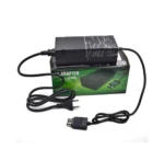 Fuente de alimentación externa negra para Xbox One, sobre su caja verde con cable incluido y conector DC visible.