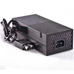 Fuente de alimentación externa negra para Xbox One, con cable enrollado y conector C14 visible en la parte trasera.