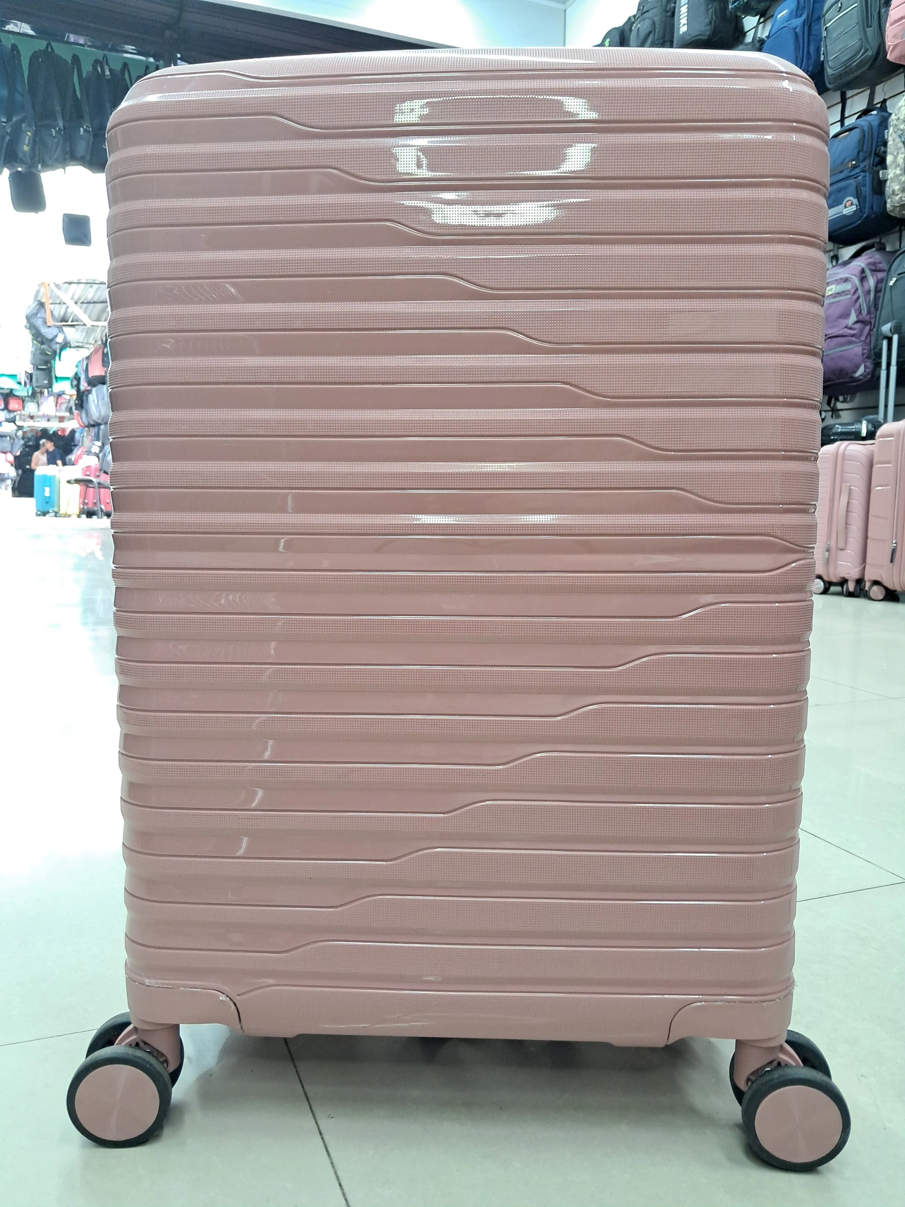 Maleta de cabina rosa con ruedas giratorias y diseño de líneas horizontales, vista frontal en tienda.