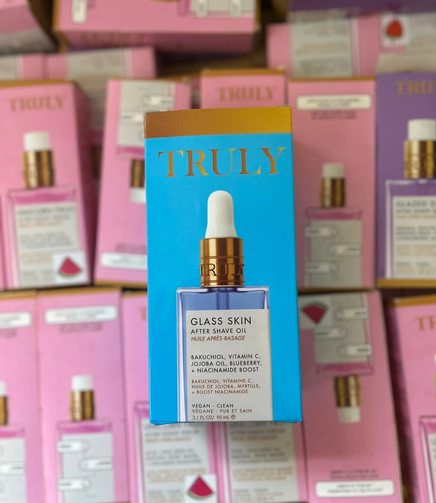 Pack de dos aceites corporales Truly Glass Skin con Bakuchiol y Vitamina C, en caja azul con detalles dorados, presentación vertical sobre estantería con productos similares en tonos rosa y morado.