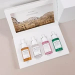 Kit de cuatro mini ampollas SKIN1004 con centella asiática, presentadas en caja blanca con tapa ilustrada. Frascos transparentes con líquidos en tonos amarillo, blanco, rosa y verde, dispuestos horizontalmente sobre fondo claro.