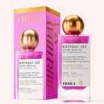 Botella de aceite corporal Truly Birthday Sex en color rosa con detalles dorados, junto a su caja. Etiqueta indica ingredientes como niacinamida, safrán y ácido hialurónico. Presentación vegana y limpia.