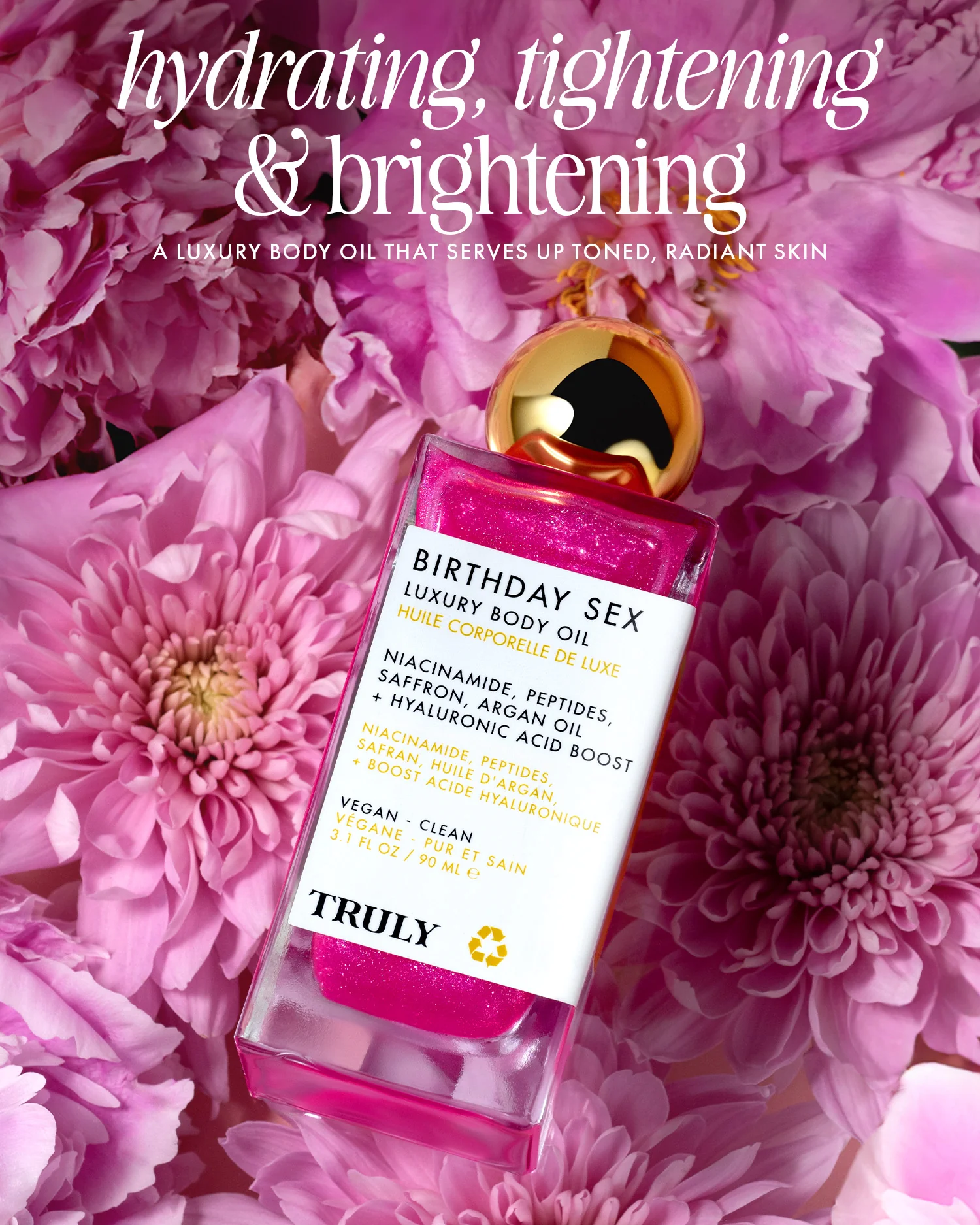 Botella de aceite corporal Truly Birthday Sex con brillo rosa, sobre flores rosadas. Etiqueta blanca con ingredientes visibles: niacinamida, péptidos, argán y ácido hialurónico. Presentación vegana y limpia.