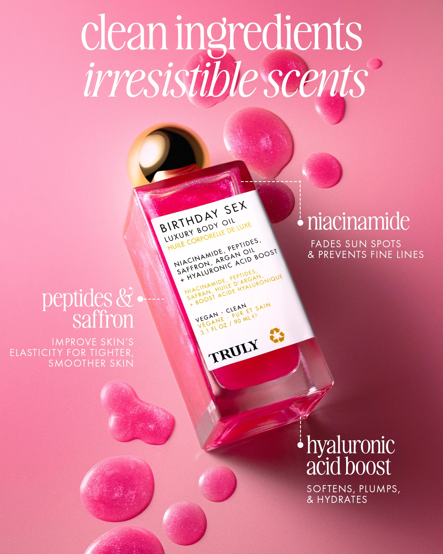 Aceite corporal Truly Birthday Sex en frasco rectangular transparente con líquido rosa brillante, rodeado de gotas del mismo tono sobre fondo rosa pálido. Etiqueta blanca con texto negro y detalles en dorado.