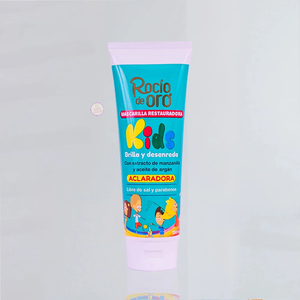 Tubo de mascarilla restauradora para niños, color azul claro con ilustraciones de personajes infantiles. Etiqueta indica “Kids”, “aclaramadora” y menciona extracto de manzanilla y aceite de argán. Presentación vertical sobre fondo blanco.