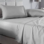 Juego de sábanas gris claro queen liso, con acabado suave y moderno, mostrando colchón, almohadas y sábanas dobladas en cama con cabecero tapizado.