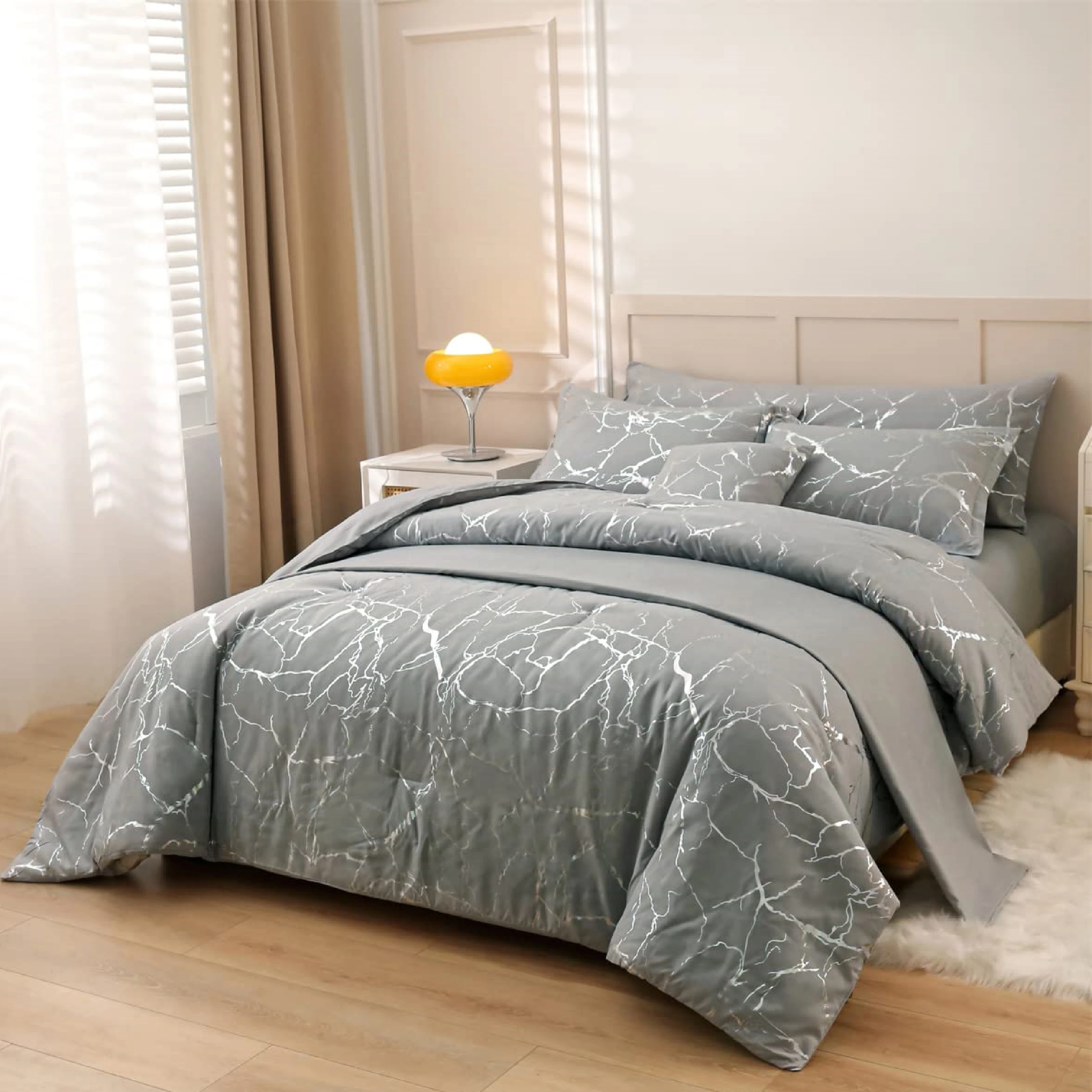 Funda duvet gris con diseño mármol plateado en cama de dos plazas, con cojines a juego y mesita lateral con lámpara amarilla al fondo.