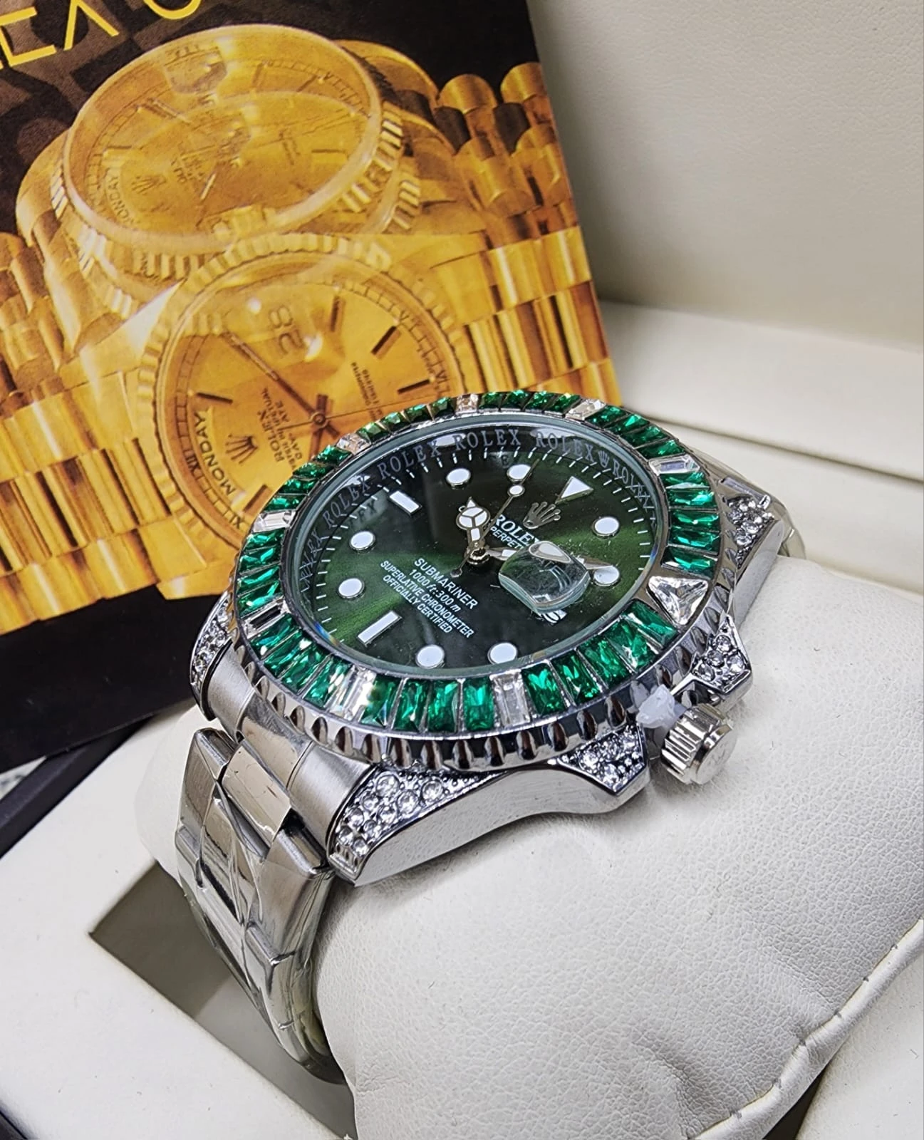Reloj de lujo con esfera análoga, correa de acero inoxidable y detalles en zafiro verde y diamantes, sobre soporte blanco.