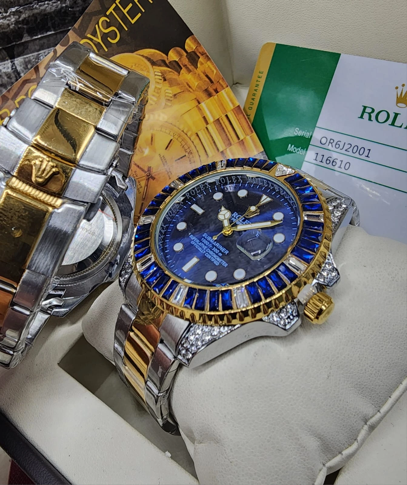 Reloj de lujo con esfera azul, detalles de zafiro y correa bicolor oro y acero, acompañado de caja y certificado.