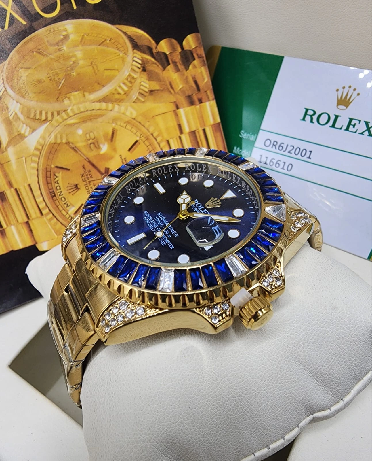 Reloj de lujo para caballero en oro amarillo con esfera análoga azul, detalles de zafiro y diamantes, sobre soporte blanco con documentación oficial.