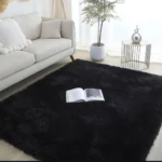 Tapete negro peludo de alta densidad en sala, con libro abierto sobre su superficie y sofá gris al fondo.
