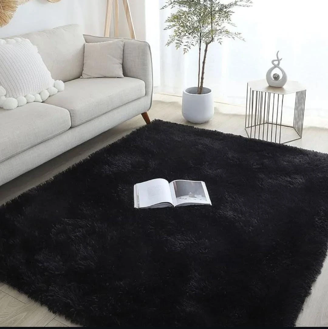 Tapete negro peludo de alta densidad en sala, con libro abierto sobre su superficie y sofá gris al fondo.