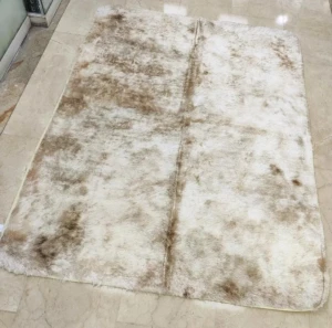 Tapete peludo grande de alta densidad en tonos beige y blanco, con textura suave y acabado natural, colocado sobre piso de baldosas claras.