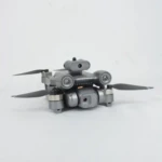 Cuadricóptero plegable gris con cámara frontal y sensores laterales para evitación de obstáculos, mostrando hélices desplegadas y estructura compacta.