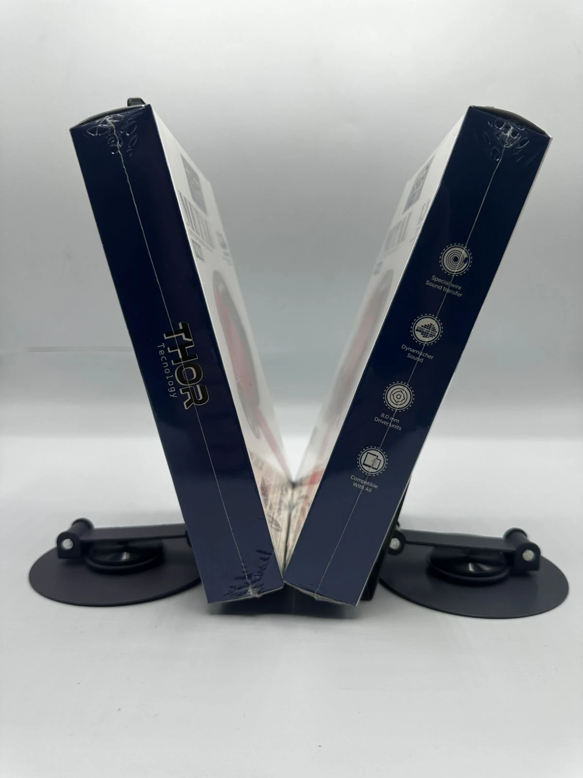 Pack de dos auriculares intrauditivos de metal en caja azul oscuro, dispuestos en forma de V sobre soporte negro.