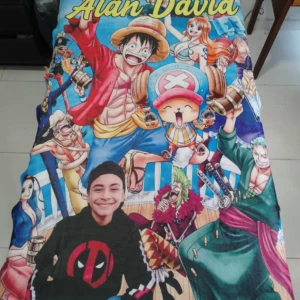 Cobija personalizada de 1,40m con diseño de One Piece y de Alan David en primer plano, bordes con personajes icónicos y fondo azul vibrante.