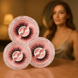 Tres pares de pestañas autoadhesivas reutilizables en estuches transparentes con fondo rosa, dispuestos en triángulo sobre superficie madera.
