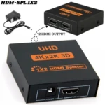 Adaptador HDMI 1x2 negro con cable de alimentación, muestra frontal y lateral con puertos de entrada y salida, etiqueta UHD 4Kx2K 3D.
