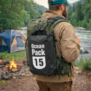 Bolso impermeable negro de 15 litros con texto blanco, usado por hombre en camping junto a río y fogata.