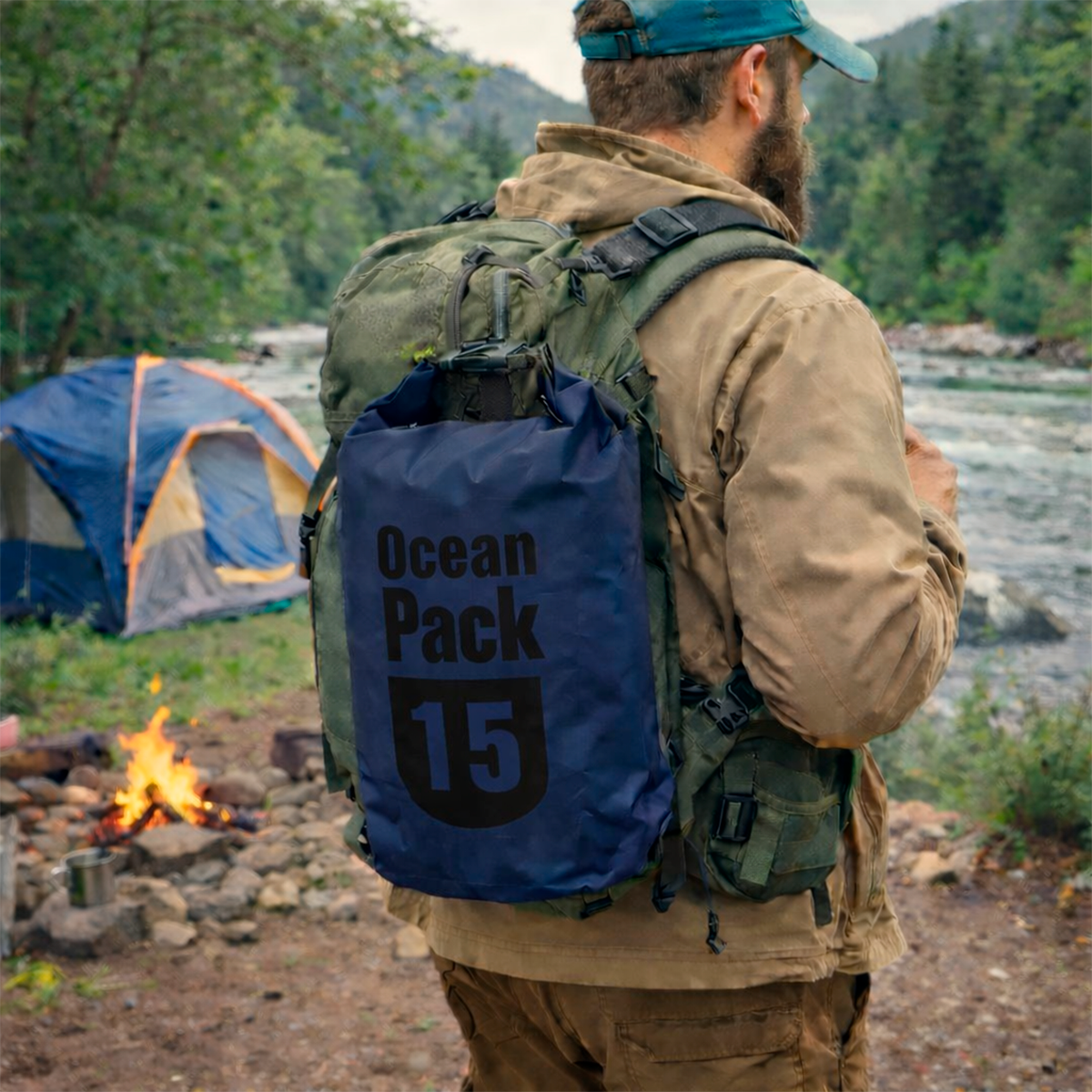 Bolso impermeable azul marino de 15 litros con texto negro, usado como mochila por hombre en camping junto a río y fogata.