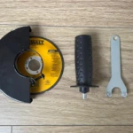 Vista superior de accesorios para pulidora Dewalt Cola Raton: disco de corte amarillo con marca, mango ergonómico negro con textura y llave de ajuste plateada, sobre superficie de madera clara.