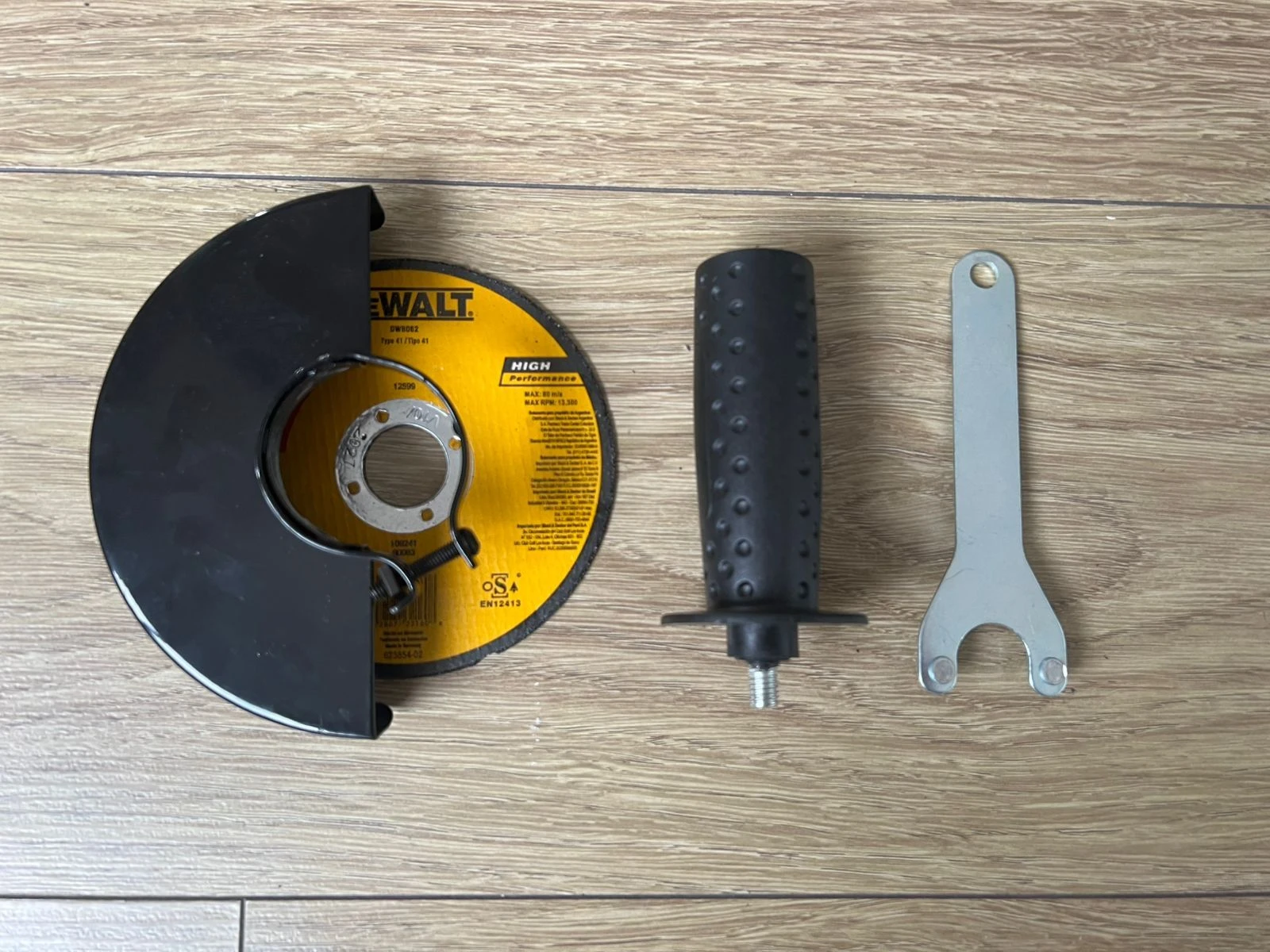 Vista superior de accesorios para pulidora Dewalt Cola Raton: disco de corte amarillo con marca, mango ergonómico negro con textura y llave de ajuste plateada, sobre superficie de madera clara.