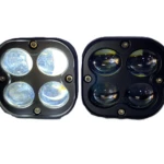 Dos faros cuadrados de exploración con cuatro lentes, uno encendido en blanco y otro apagado en amarillo, montados sobre carcasa negra.