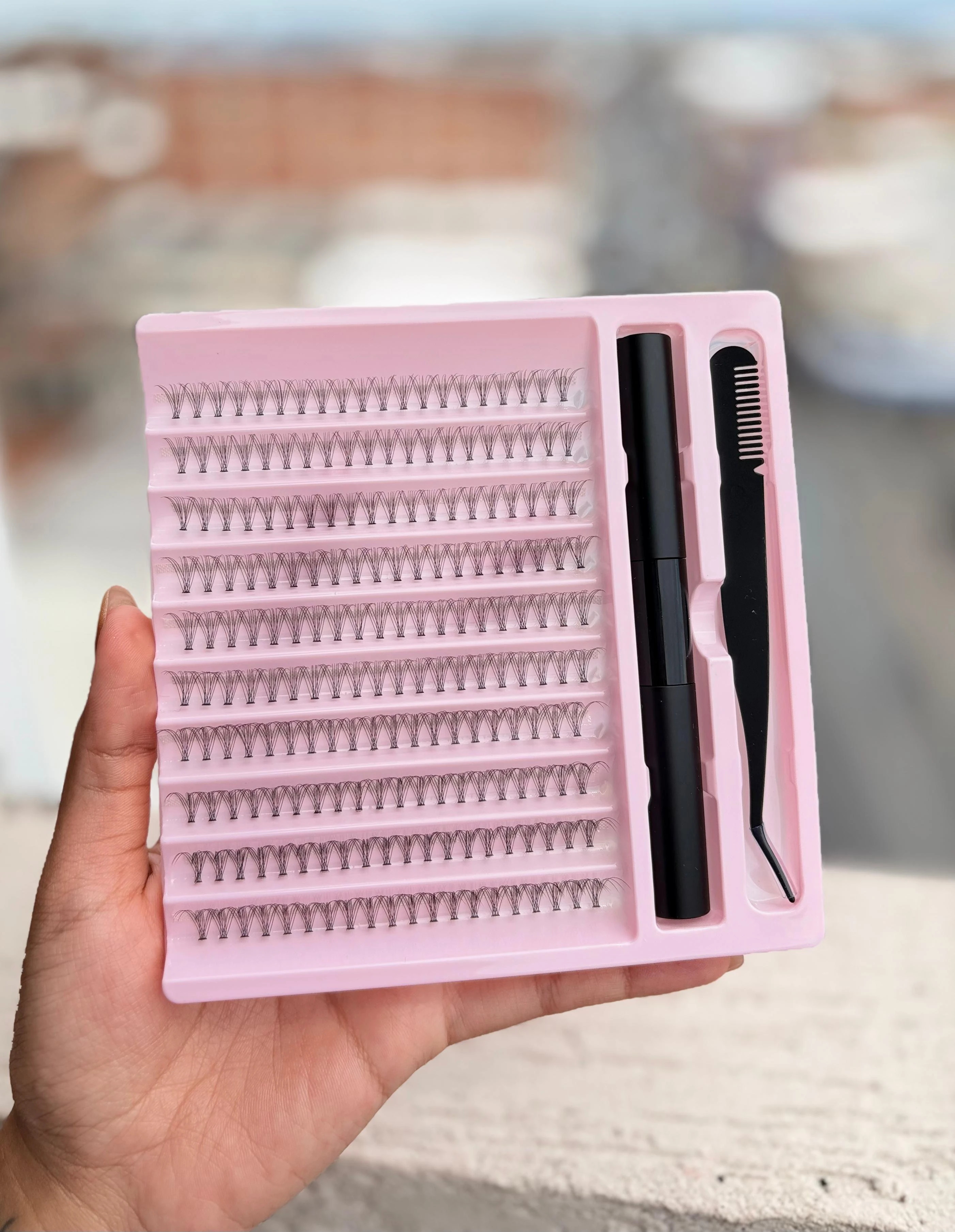 Set de pestañas postizas en abanico preformado en estuche rosa con pinzas y cepillo, mostrando filas organizadas de pestañas individuales.