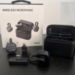 Caja de producto inalámbrico modelo SX38 con estuche de carga negro abierto, micrófono y accesorios dispuestos sobre superficie oscura.