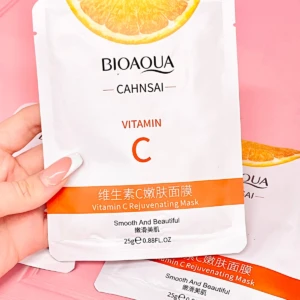 Mano sosteniendo mascarilla facial BIOAQUA con Vitamina C, diseño blanco con naranja y texto en español e inglés, peso neto 25g.