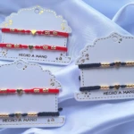 Set de pulseras artesanales para mujer con dijes de corazón y cuentas doradas, disponibles en hilos rojo y negro sobre tarjetas de presentación blancas.
