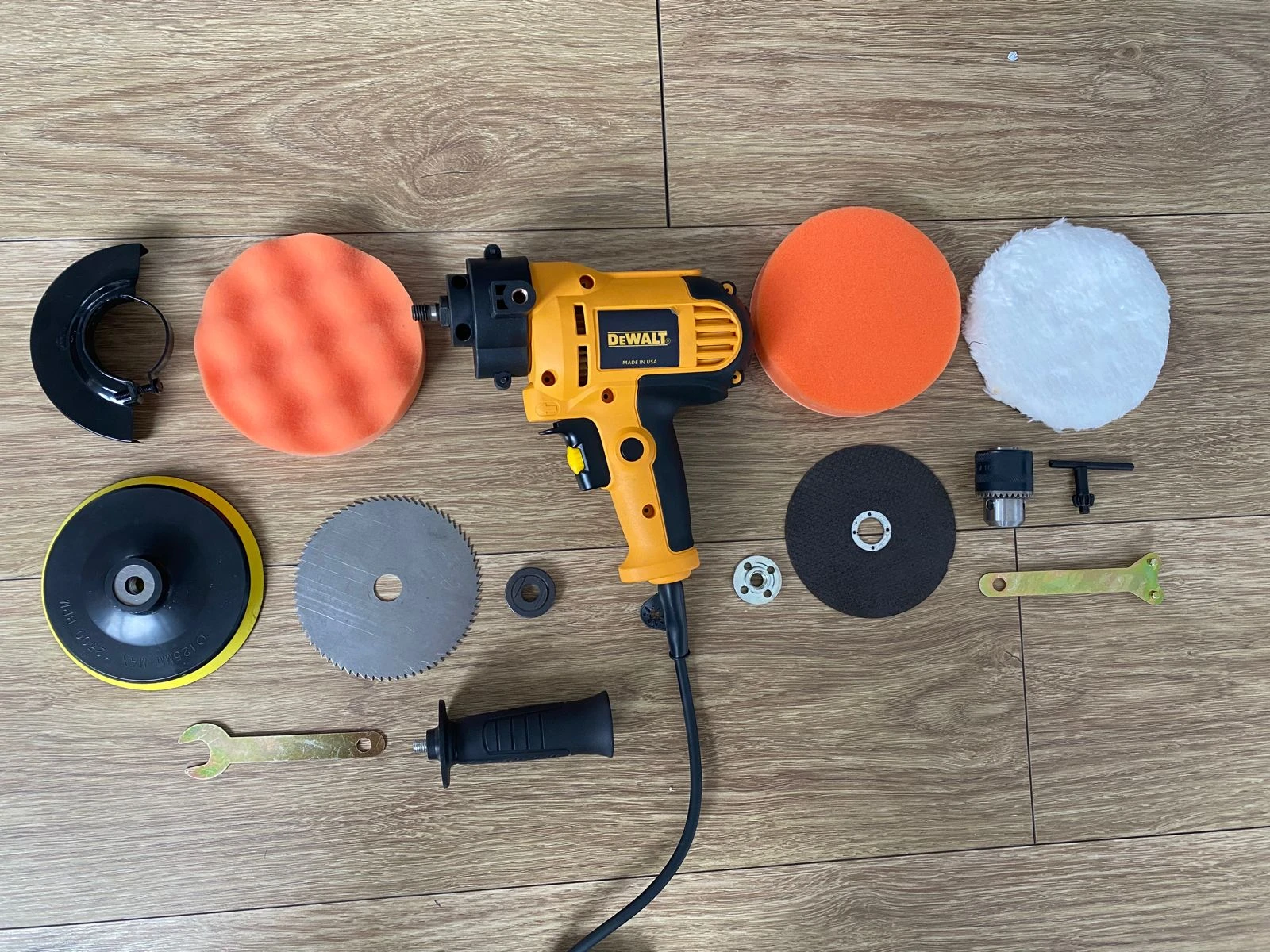 Polichadora Dewalt amarilla con accesorios incluidos: discos de corte, pulidores naranjas y blancos, cepillo, llaves y mango extra, dispuestos sobre superficie de madera.