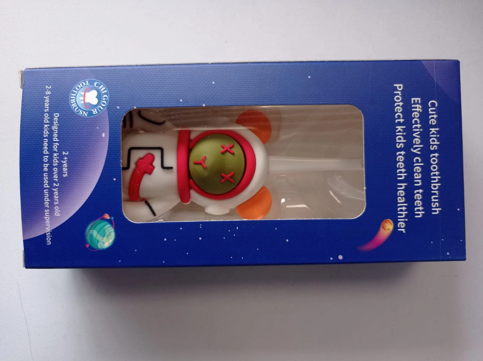 Cepillo dental infantil con diseño de astronauta, empaquetado en caja azul con ventana transparente que muestra el producto.
