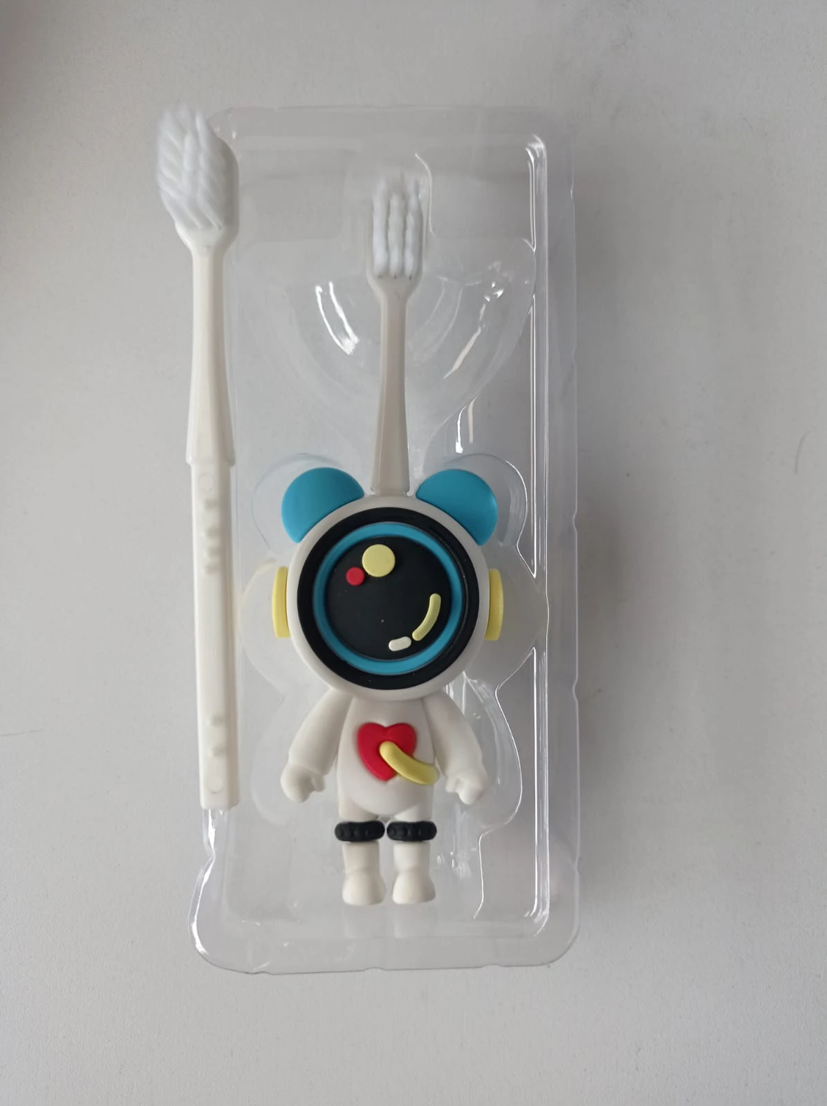 Pack transparente con tres cepillos de dientes blancos para niños, uno con diseño de astronauta sonriente y otro con cerdas visibles, presentados en empaque individual.