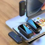 Microfono solapa doble USB-C en negro, mostrando tres unidades: una conectada a smartphone, otra sobre laptop y tercera en primer plano, con luces verdes activas.