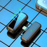 Microfono solapa doble USB-C en color negro, con indicador LED verde y conector Lightning visible, sobre superficie azul con reflejos.