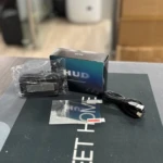 Pack de velocímetro proyector digital LED para parabrisas, con caja, cable USB y accesorios en bolsa plástica, sobre superficie oscura con texto parcialmente visible.