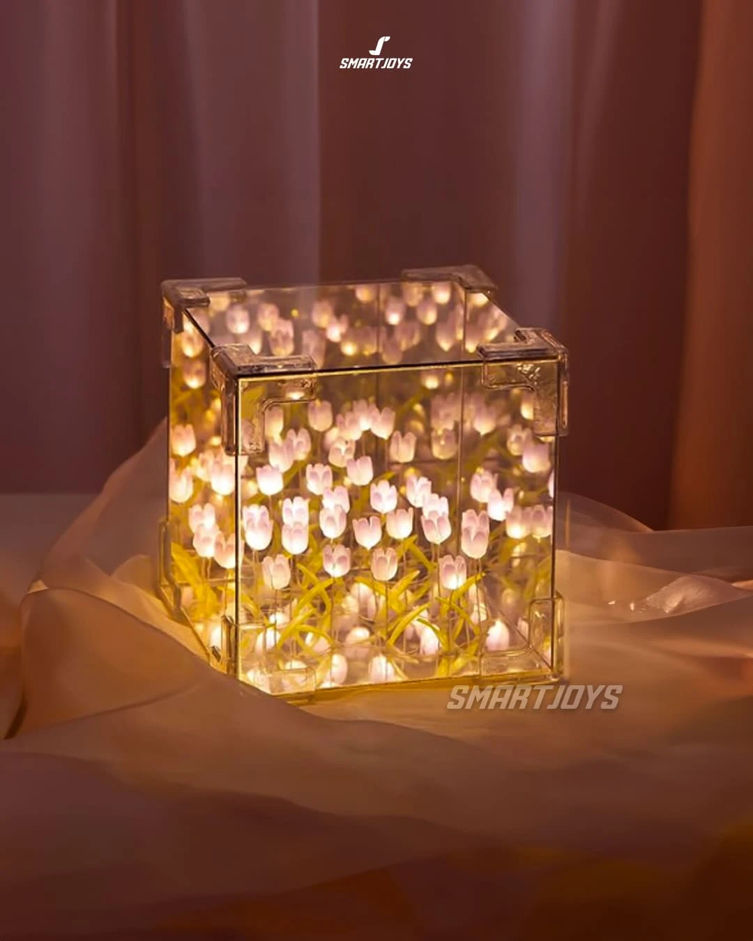 Lámpara cúbica de tulipanes con luz LED cálida, efecto espejo infinito, sobre tela suave en tono rosado.