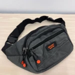 Canguro gris oscuro con tres compartimentos, correa ajustable y detalles en naranja; ideal para llevar activos durante actividades deportivas.
