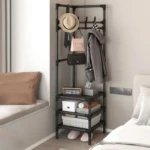 Perchero metálico negro en esquina, con perchas, estantes y cesta; muestra sombrero, bolso, abrigo, reloj digital y calzado. Ideal para organizar espacios reducidos.