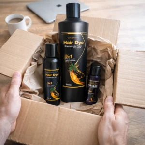 Caja abierta mostrando tinte para cabello en tres presentaciones: botella grande negra con etiqueta dorada, dos frascos más pequeños, uno negro y otro azul oscuro, todos con diseño de piña y texto visible.