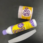 Kit de uñas en acrílico con polvo y monómero, presentados en envases amarillos y morados sobre superficie oscura. Incluye lija blanca para acabado final.