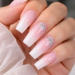 Manicura con uñas largas en forma de almendra, degradado de blanco a rosa pálido, con detalles de glitter plateado en dos dedos.