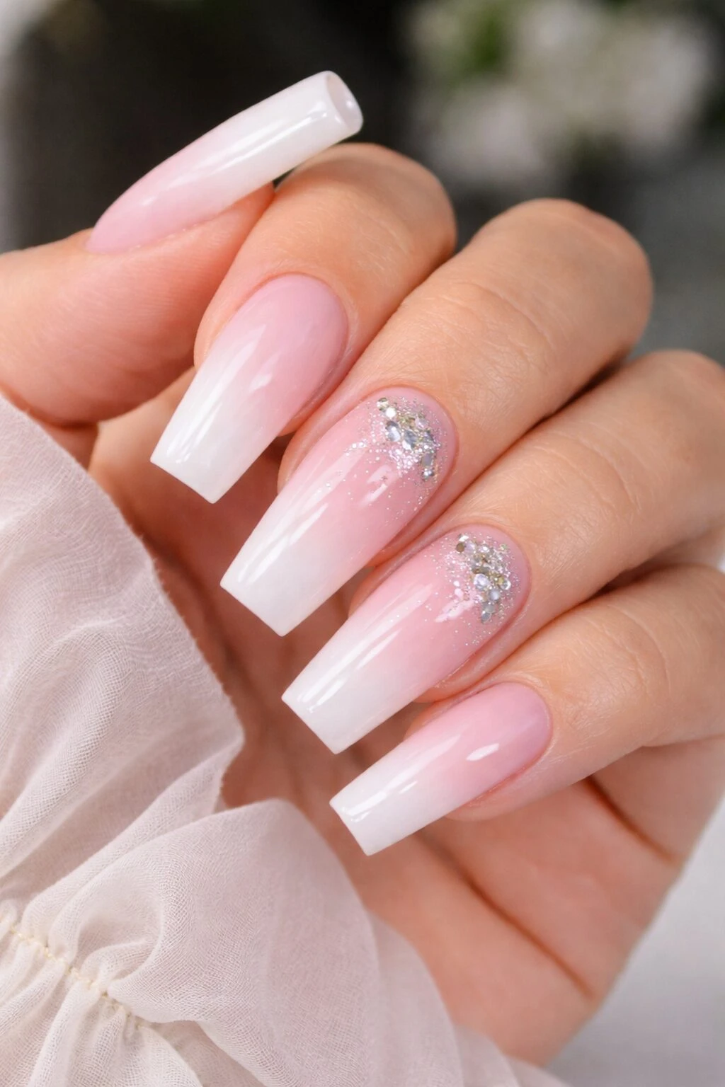 Manicura con uñas largas en forma de almendra, degradado de blanco a rosa pálido, con detalles de glitter plateado en dos dedos.