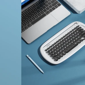 Teclado inalámbrico Remax de color blanco con teclas negras, sobre superficie azul junto a laptop, smartphone y stylus.